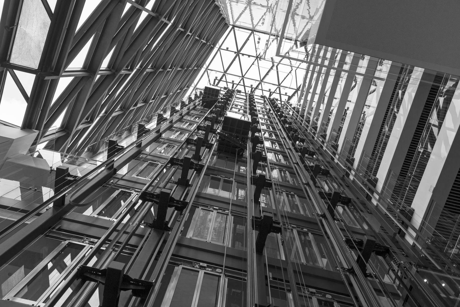 Looking up through a glass atrium at a bank of elevator hoistways