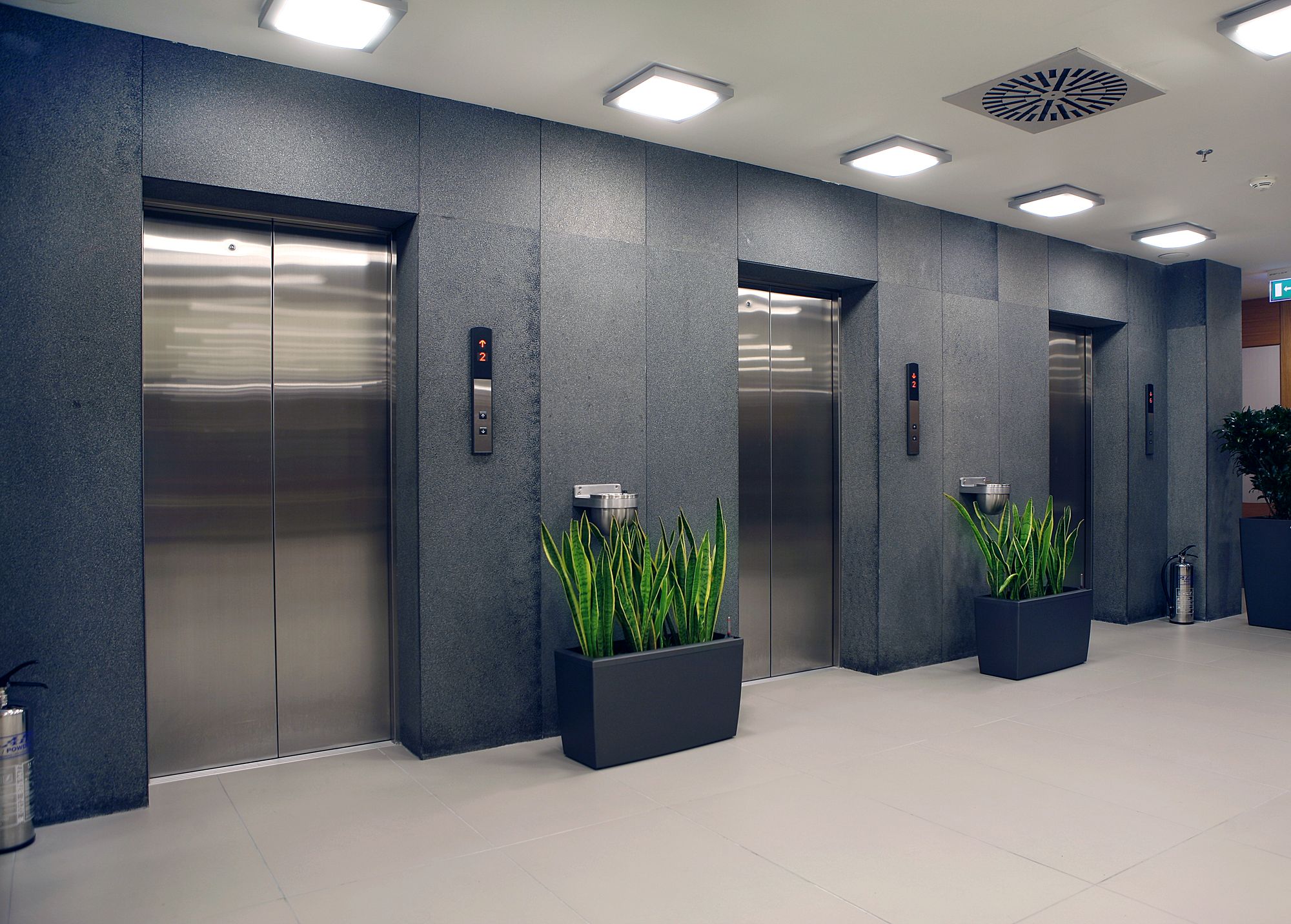 A row of stainless-steel elevator doors in a granite lobby