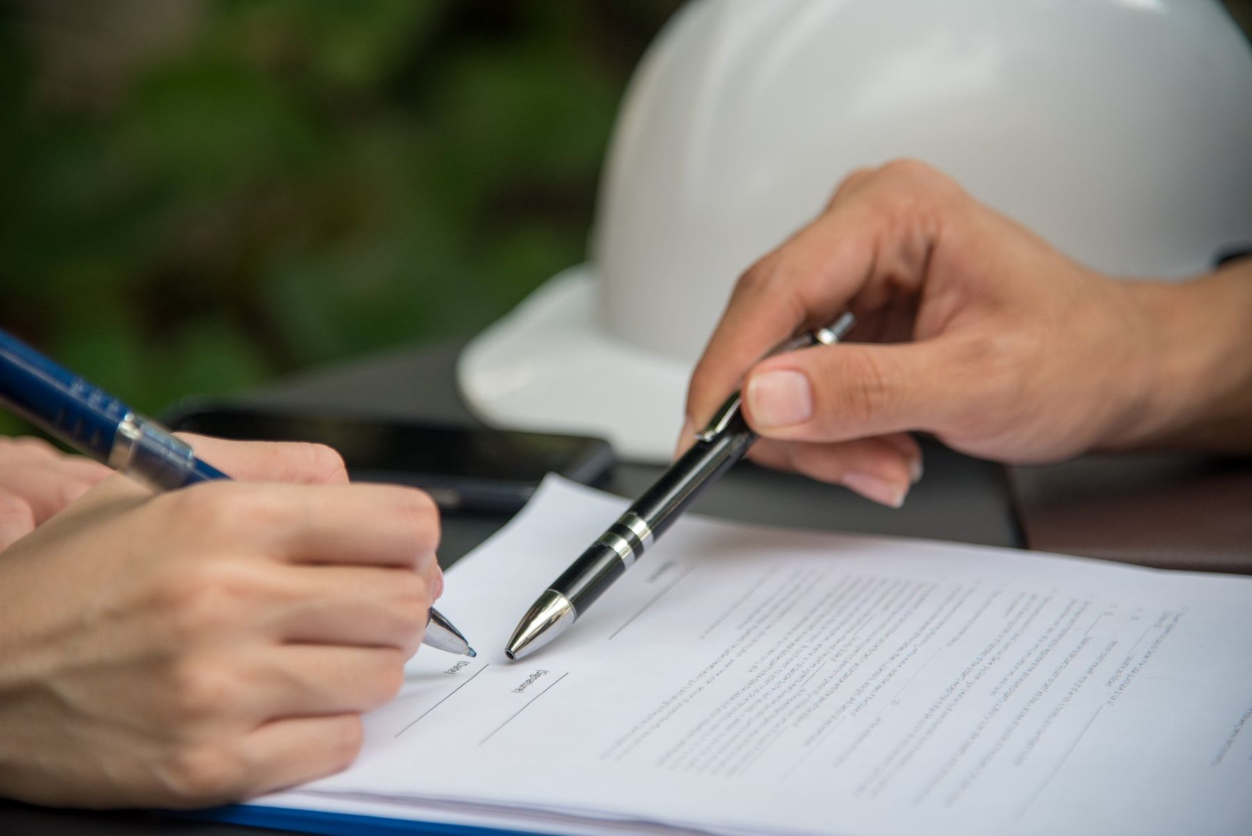 Two people signing a construction contract beside a hard hat
