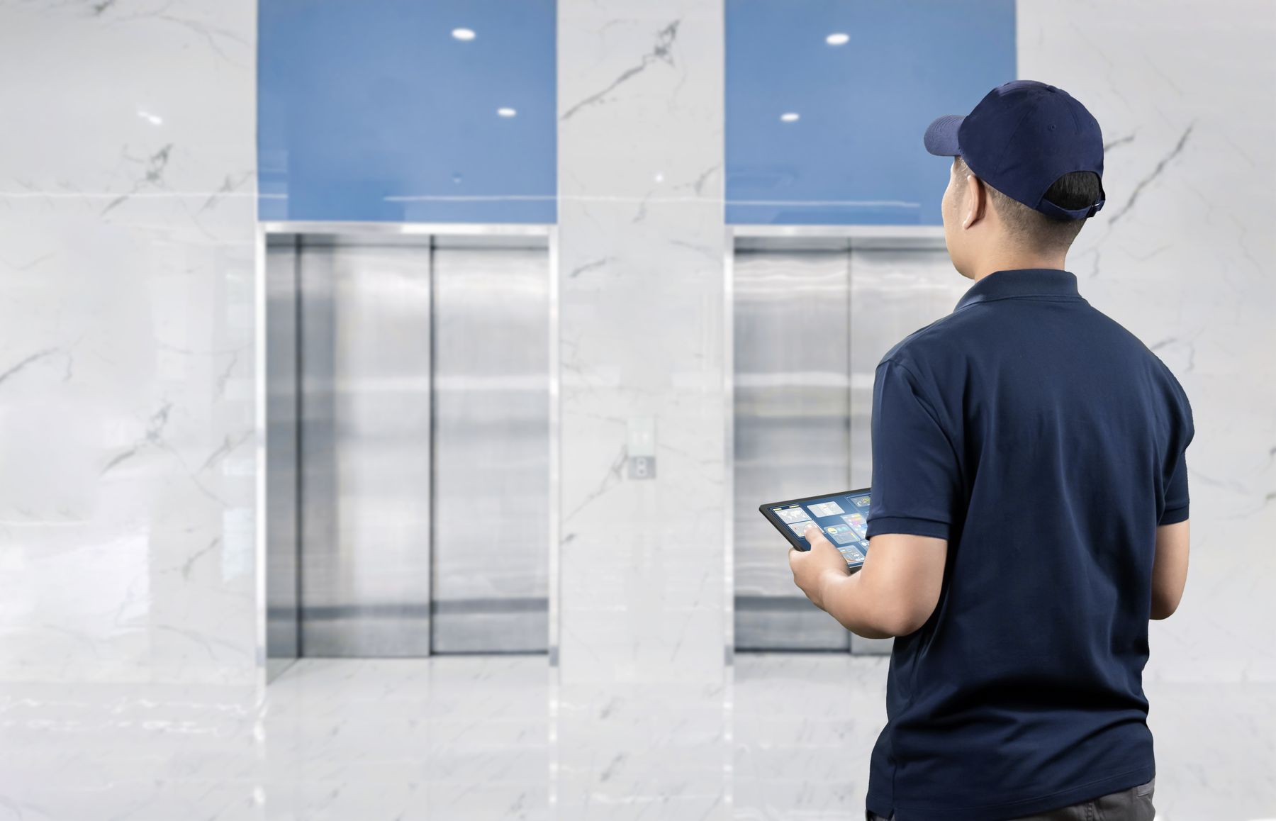 A technician with a tablet checking a bank of elevators
